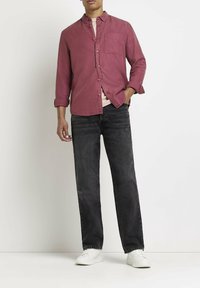 Camicia button-up rosa chiaro con maniche lunghe, abbinata a jeans grigio scuro e sneakers bianche. Presenta una tasca frontale sulla camicia.