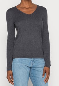 Pull à col en V gris foncé à manches longues, en tissu doux et texturé, associé à un jean bleu clair. Caractéristiques : poignets et ourlet côtelés.