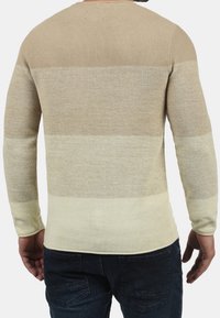 Pull beige en maille avec des rayures horizontales dans différentes nuances de beige et de crème, manches longues et col rond.