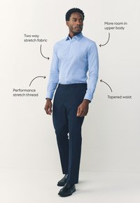 Camicia azzurro chiaro a bottoni con righe, realizzata in tessuto elasticizzato bidirezionale; abbinata a pantaloni sartoriali blu scuro, con vita sagomata.