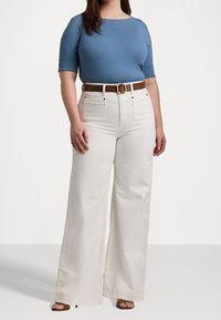 Ljust blått åtsittande linne med korta ärmar, kombinerat med vita vida byxor och ett brunt bälte med en fyrkantig guldbälteknäppning. Bruna klacksandaler.