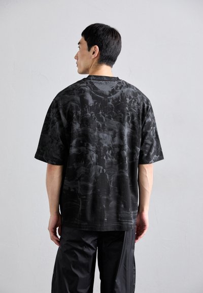 Camiseta negra de gran tamaño con un patrón gráfico texturizado, mangas cortas y cuello redondo, combinada con pantalones negros de corte holgado.