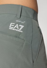 Γκρι αθλητικά σortς με λεία υφή, πλαϊνές τσέπες και άσπρη επωνυμία "EA7 EMPORIO ARMANI" με "VENTUS7" από κάτω.