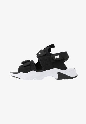Sandalia deportiva Nike en blanco y negro con correas ajustables y suela acolchada, vista lateral sobre fondo blanco liso.