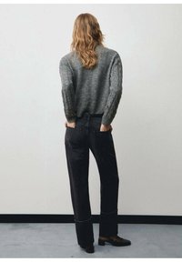 Grauer gestrickter Pullover mit strukturierten Ärmeln, kombiniert mit hochgeschnittenen schwarzen Jeanshosen in lockerer Passform und sichtbaren Nähdetails.