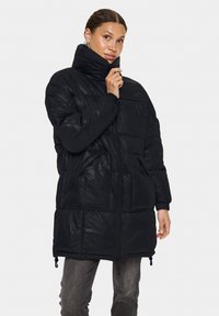 Svart puffjacka med hög krage, dragkedjestängning, elastiska mudd och två framfickor. Glansig yta och isolerat design för värme.