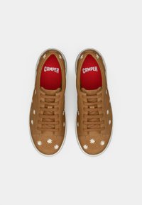 Bruna lädersneakers med vita blommönster, röda innersulor och vita gummisulor, med fem par hål för skosnören.