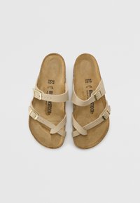 Beige avosut sandaalit, joissa on kaksi säädettävää nahkahihnaa ja kultaiset soljet, sekä ruskea korkkipohja ja teksturoitu pohja.