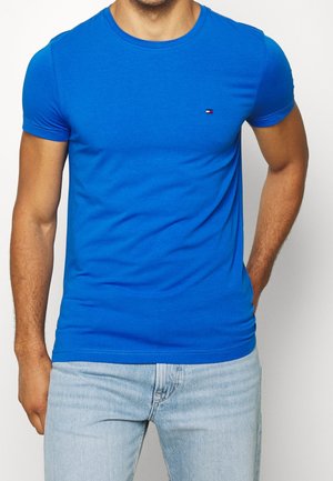 Blue cotton t-shirt with short sleeves, crew neck, slim fit, featuring a small logo accent on the chest, paired with light blue jeans.