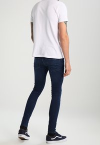 Mörkblå skinny jeans, blandning av bomull, med subtila blekningar. Bärs med en enkel vit t-shirt och svarta sneakers med vita detaljer.