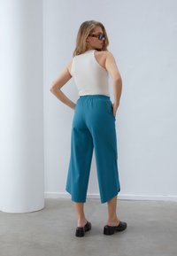 Aqua fargede vide benbukser laget av lett stoff med elastisk midjebånd. Kombinert med svarte hælhogger og en tettsittende beige topp.