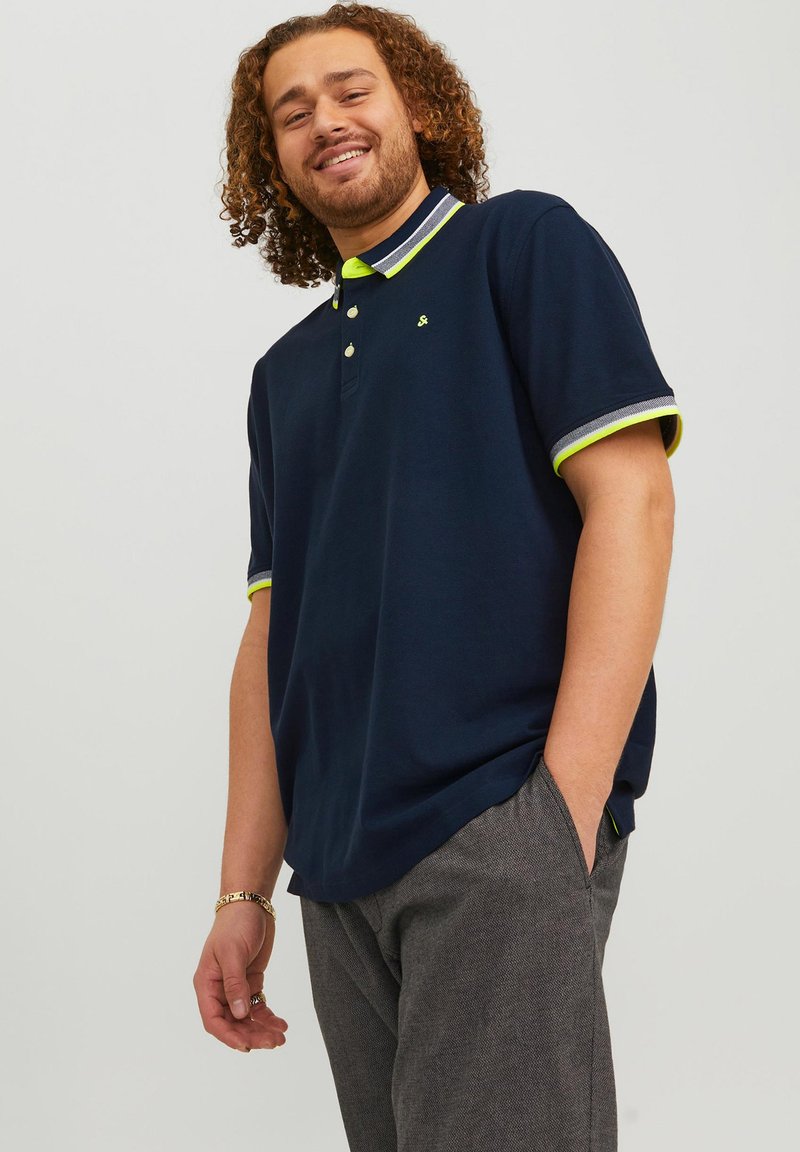 Marineblauwe poloshirt met een gele accentkraag en manchetten, voorzien van drie knopen. Glad katoen met een normale pasvorm en korte mouwen.