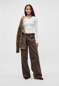 Šviesiai pilka ilgomis rankovėmis palaidinė derinama su rudomis plačiomis kelnėmis. Modelis laiko rudą švarką; juodas diržas su metaliniais apskritimais. Lygios tekstūros.