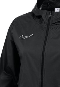 Giacca Nike nera con cappuccio, caratterizzata da un logo bianco sul petto, chiusura con zip e una texture di tessuto liscia e leggera.