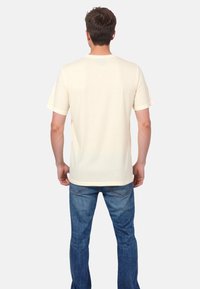 Lys gul t-shirt lavet af blødt stof, med korte ærmer, rund halsudskæring og en afslappet pasform, parret med blå jeans.