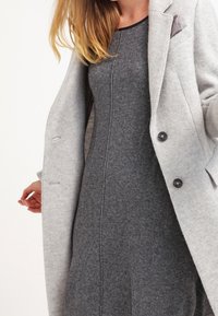 Sukienka z mieszanki wełny w kolorze szarym o dopasowanym fasonie, zestawiona z jasnoszarym płaszczem z czarnymi guzikami i akcentem w postaci kieszeni.