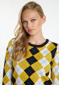 Maglione giallo e nero a motivo argyle con dettagli blu, caratterizzato da un collo nero rotondo e un tessuto morbido e testurizzato.