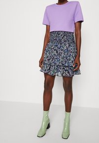 Fialový top s krátkým rukávem v kombinaci s květinovou vrstvenou mini sukní v tmavě modré a zelené barvě, doplněný lesklými zelenými kotníkovými botami.