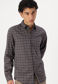 Button-up skjorte med et mørkt ternet mønster med lilla og hvide accenter. Fremstillet af et blødt stof, lange ærmer og buet kant.