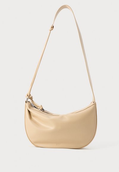 Bolso de hombro de cuero beige con forma curva, detalle de nudo ajustable en la correa y cierre de cremallera. Sutil logo en relieve en la parte frontal.