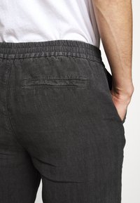 Černé lněné kalhoty s elastickým pasem, které mají zadní kapsu a mírně texturovaný povrch.