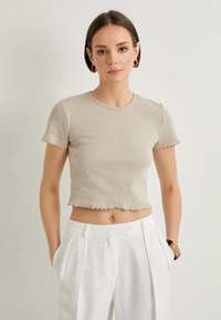 Top corto acanalado beige con mangas cortas y dobladillo sin terminar, combinado con pantalones de pliegues blancos de cintura alta. Textura suave, diseño simple.