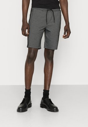 Grijze jersey shorts met een elastische tailleband en een trekkoord. Voorzien van zijzakken en een comfortabele pasvorm, gecombineerd met zwarte schoenen en sokken.