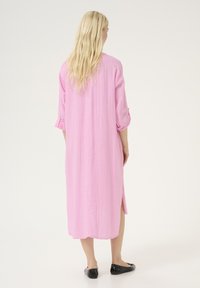 Garš roze kleita no viegla auduma, ar sarullētām piedurknēm un sānu šķēlumiem, taisnas griezuma un maigas tekstūras.