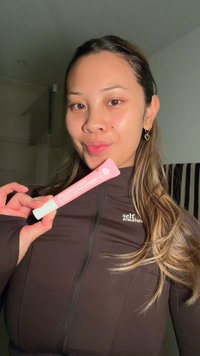 Kvinna med långt hår håller en rosa hyaluronsyraskincare-tub, klädd i en mörk zip-up tröja med texten "self Athletics".