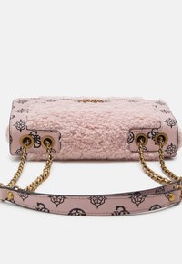 Sac à main rose texturé avec motif logo noir, bandoulières chaîne dorée passant par des œillets dorés, et bandoulière assortie avec clous dorés.