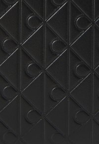 Black textured surface with raised diamond shapes and semi-circular indentations patterned in a grid formation.