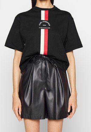 Mujer con una camiseta negra de Karl Lagerfeld con rayas verticales rojas y blancas y pantalones cortos de cuero negros de talle alto con un cinturón atado.