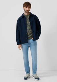 Granatowa kurtka na guziki narzucona na wielokolorowy, dziergany sweter, w połączeniu z jasnoniebieskimi dżinsami i szarymi butami sportowymi. Prosty, nowoczesny design.