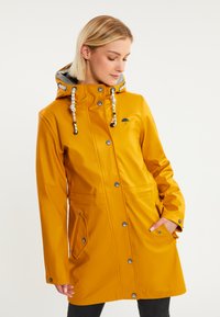 Chubasquero amarillo impermeable con un diseño ajustado, botones a presión, capucha con cordón y bolsillos laterales. Presenta un logo de paraguas negro en el pecho.