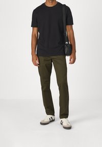 Svart t-shirt med kort ärm, olivgröna raka byxor och vita sneakers med svarta ränder, i kombination med en liten svart crossover-väska.