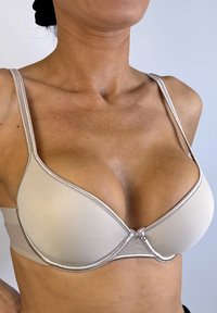 Sostenedor acolchado beige con una textura suave, soporte con aros, tirantes ajustables y detalles en borde plateado. Cuenta con un cierre de gancho y ojal.