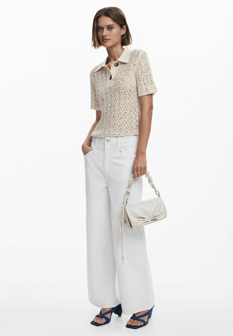 Knit polo shirt in cream with textured pattern, paired with wide white pants and a soft, bow-accented cream handbag. Blue heeled sandals.