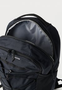 Μαύρο σακίδιο από πολυέστερ με κύριο διαμέρισμα με φερμουάρ, ελαστικό σύστημα μπάντζι μπροστά και δίχτυα στα πλαϊνά τσέπες. Στο εσωτερικό διαθέτει γκρι επένδυση.