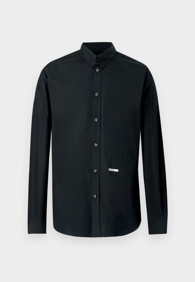 Chemise noire à manches longues en tissu lisse. Dotée d'un col boutonné, de boutons sur le devant et d'une petite étiquette logo en bas à gauche.