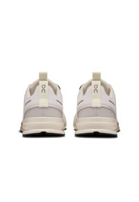 Scarpe sportive beige con tomaia in rete, design minimalista e tacco arrotondato. Presentano un'etichetta a soffietto e un branding discreto sul tacco.