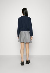 Giacca cropped blu navy con vita elastica, abbinata a una gonna grigia con motivo a diamante. Scarpe nere chunky completano il look.