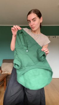 Fato de treino verde feito de material suave, com decote em V, mangas curtas e um grande bolso frontal. Apresenta um design casual com um corte ligeiramente oversized.