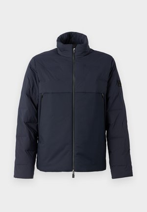 Veste en duvet bleu marine avec col montant, fermeture éclair à l'avant et poche poitrine horizontale. Texture de tissu lisse, avec un logo sur la manche.