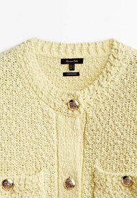 Żółty dziergany kardigan z teksturowanym wzorem, okrągłym dekoltem, dwiema przednimi kieszeniami i płaskimi srebrnymi guzikami. Metka widoczna wewnątrz.
