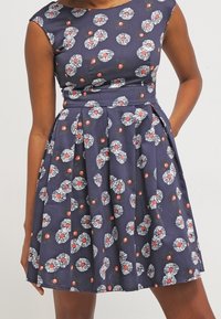 Námořnické šaty s květinovými vzory, krátkými rukávy, přiléhavým korzetem a skladanou sukní. Vyrobeno z lehkého materiálu s hladkou strukturou.