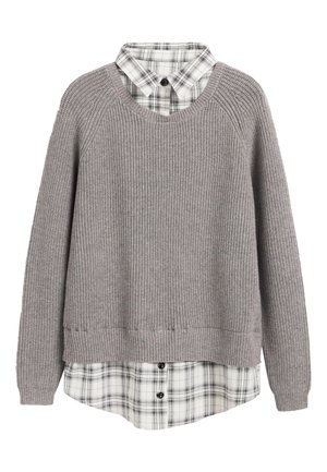 Pull en maille côtelée gris clair superposé sur une chemise à carreaux blanche et noire avec col et manches longues sur fond blanc.