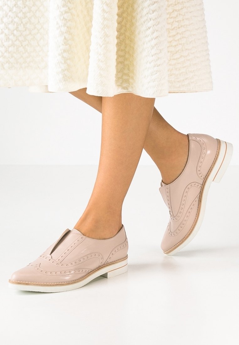 Mocassins en cuir rose clair avec un motif perforé décoratif, talon bas et semelle blanche. Présente un design découpé le long de l'empeigne.