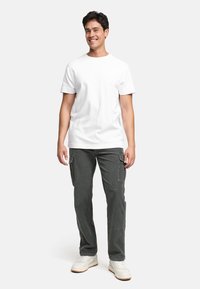 Hvit bomulls T-skjorte paret med grå corduroy cargo-bukser som har sidelommer. Modellen har på seg hvite joggesko mot en nøytral bakgrunn.