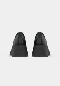 Black faux leather platform shoes with a smooth finish, rounded toe, and solid thick sole. Features minimalistic design and clean lines.