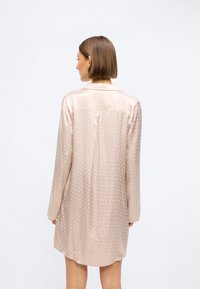 Rochie din mătase de culoare bej deschis, cu un model delicat de diamante, mâneci lungi, guler și un pliț la spate pentru o mișcare suplimentară.